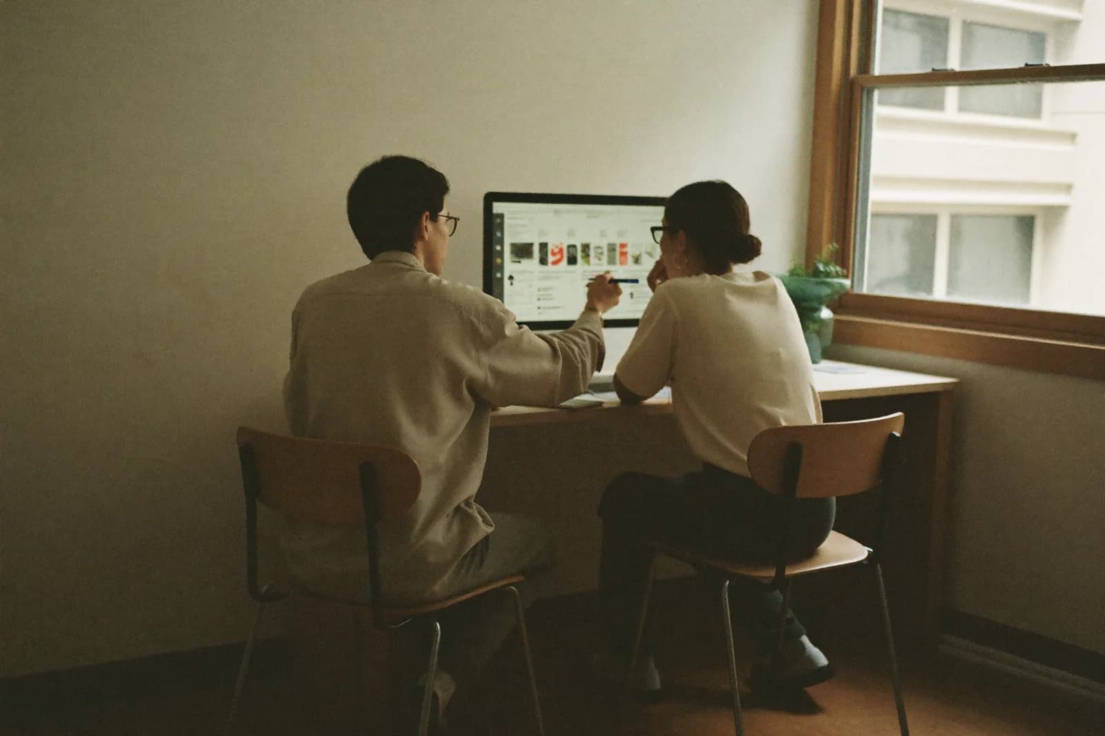 Two people talking across a workshop bench, one holding a clipboard, the other in a work apron.