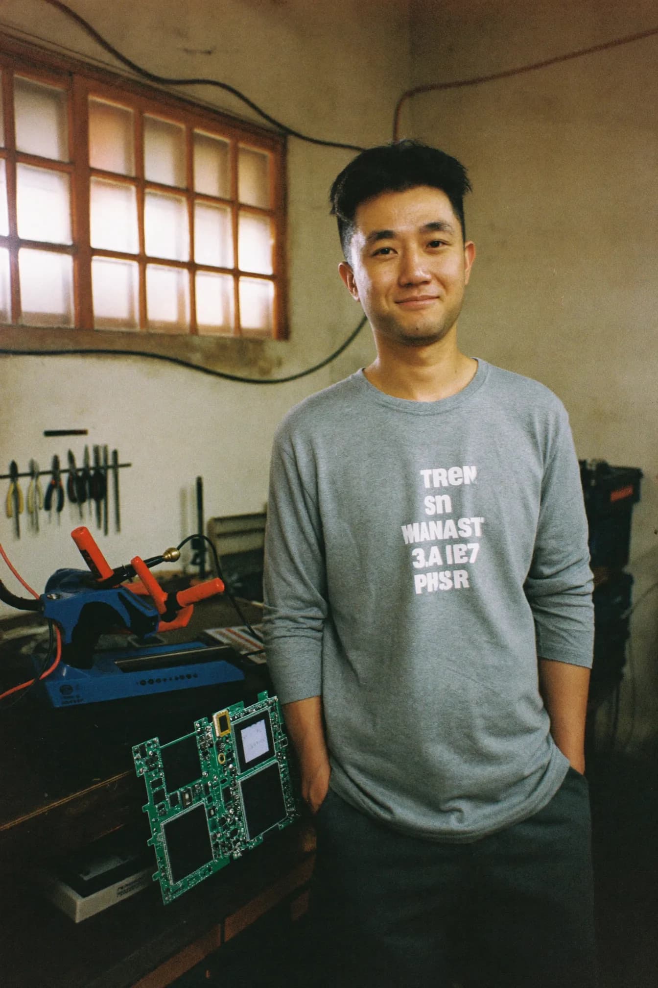 Joon Park holding a small anodized aluminium light meter, with a tray of circuit boards and a set of extruded housings on the bench in front of him.
