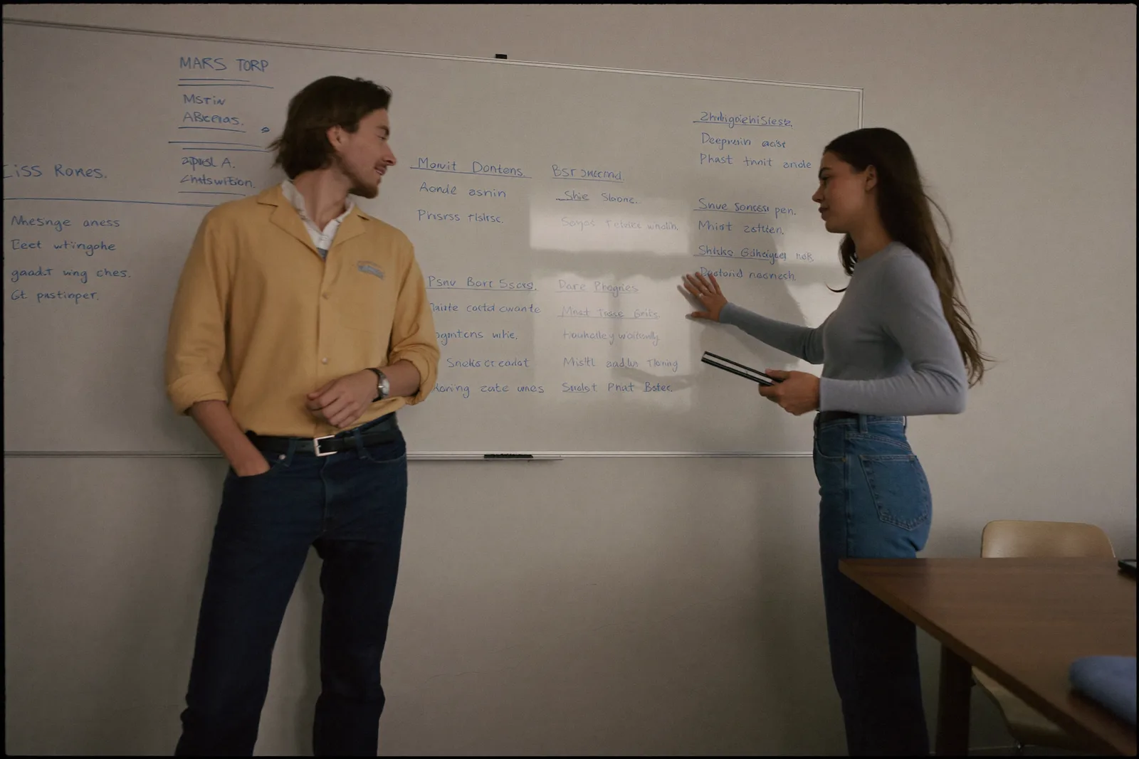 Ana Ferreira and Tom Aldous standing at a whiteboard covered in handwriting, mid-discussion.