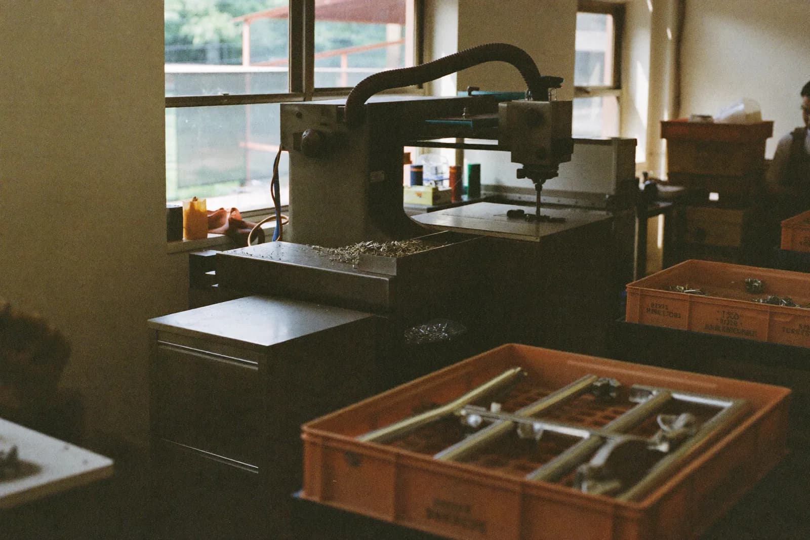 The interior of a small factory in a converted shopfront, with workbenches and machinery beneath a high storefront window.