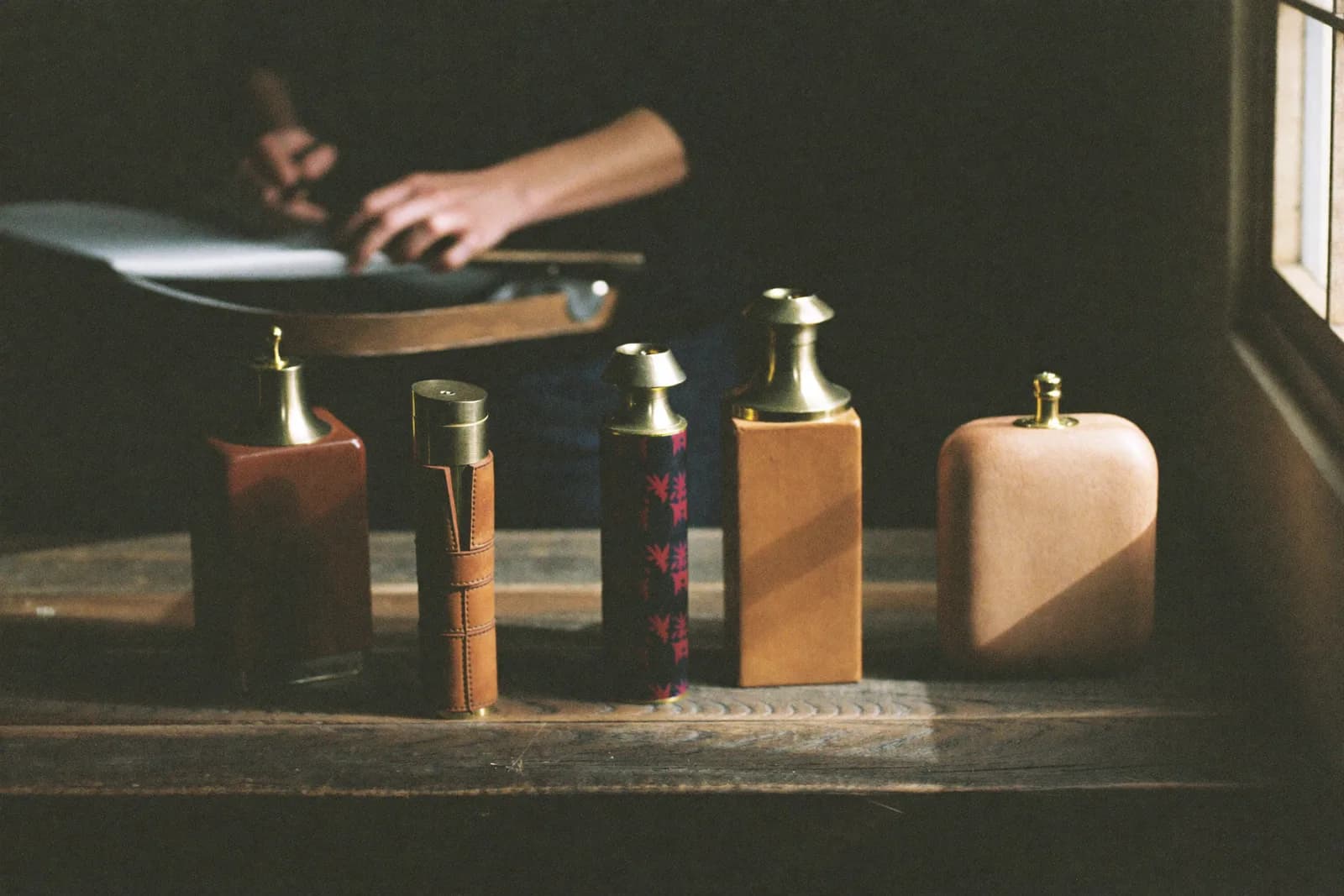 A studio workspace with finished leather and brass goods arranged on a wooden table.