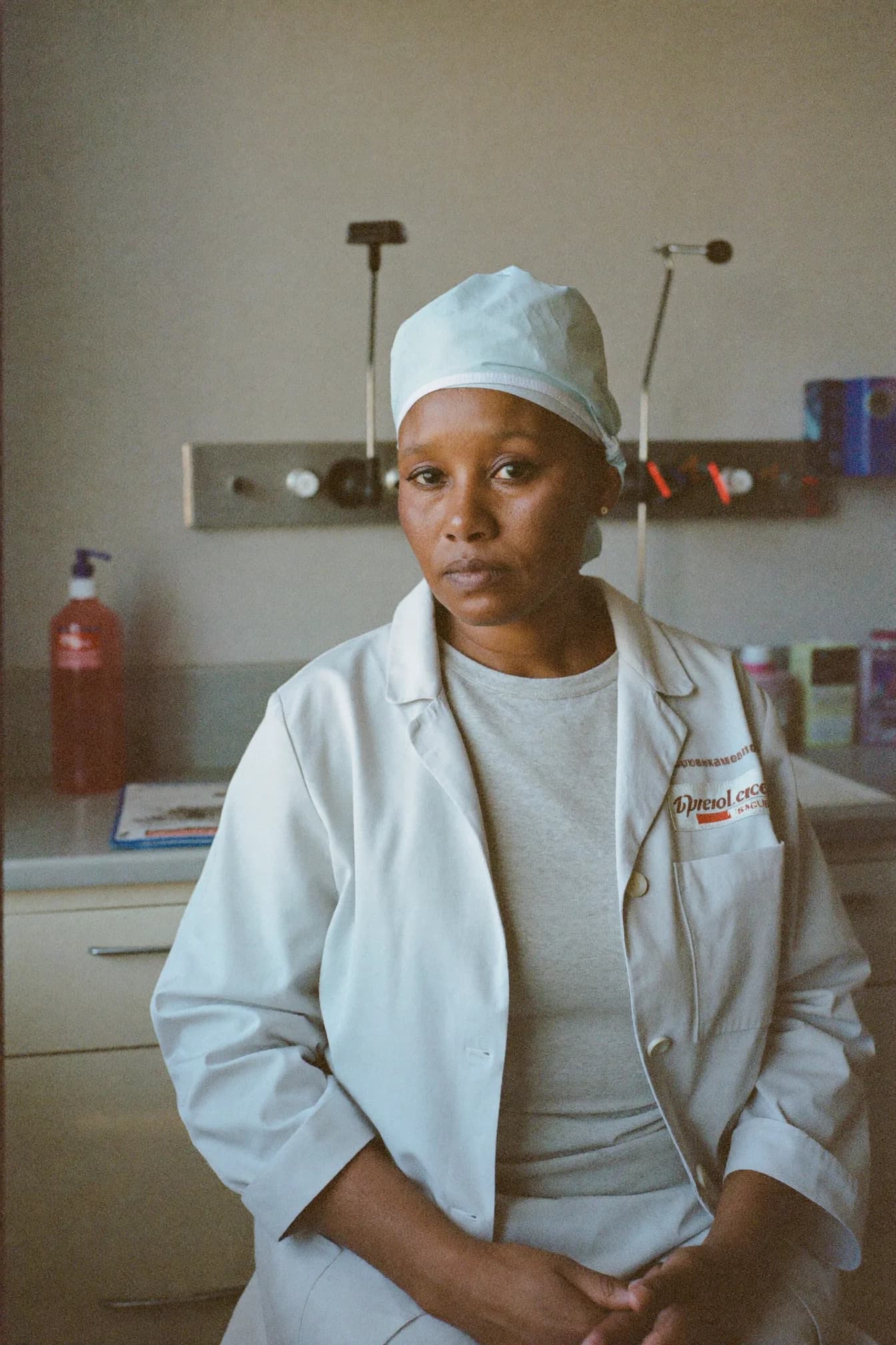 Rosalind Achebe in a lab coat at a bench, holding a small plastic test cartridge up to the light beside a bench-top reader.